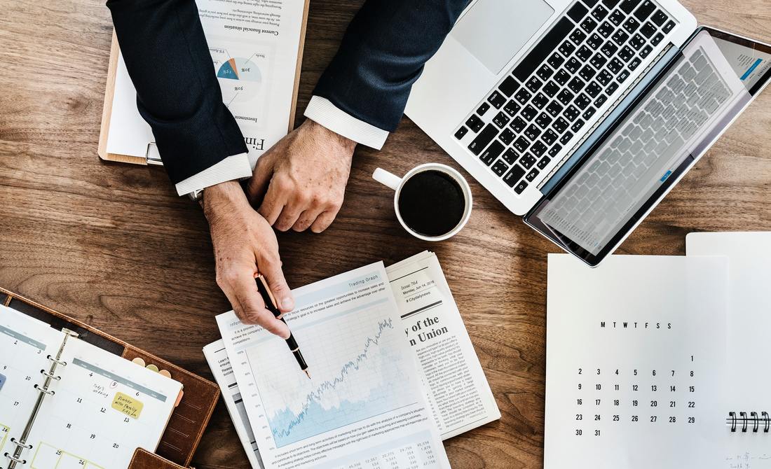 Business professional analyzing charts and reports on a desk, featuring a laptop, coffee cup, and planner, highlighting financial productivity.