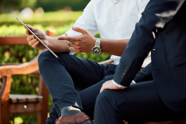 Two men engage in a discussion while reviewing content on a tablet in a garden setting, emphasizing collaboration and modern communication.
